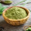 A bowl of green barley grass powder with fresh barley leaves on a rustic wooden table, highlighting the benefits of barley grass powder for health.